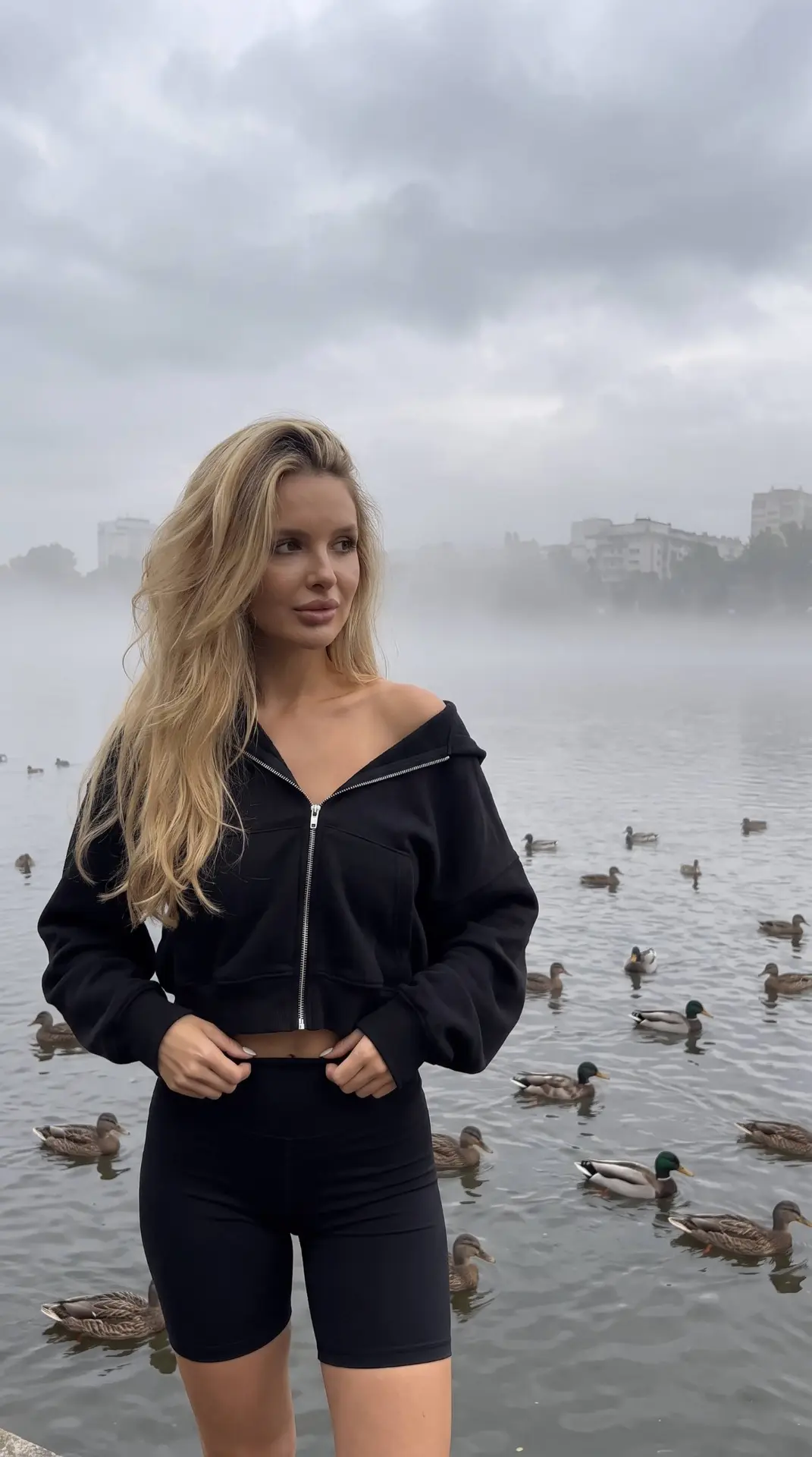На этом фото изображена молодая женщина, стоящая на фоне водоема. Девушка с длинными объемными волос