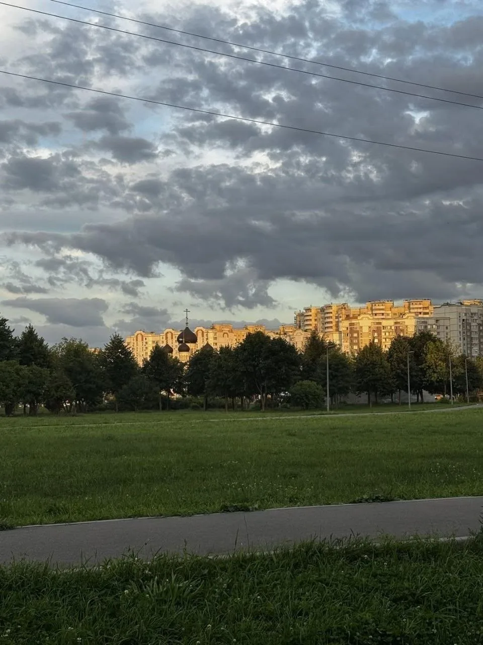 Солнце пробивается сквозь облака и подсвечивает крыши домов, а среди деревьев виднеется...