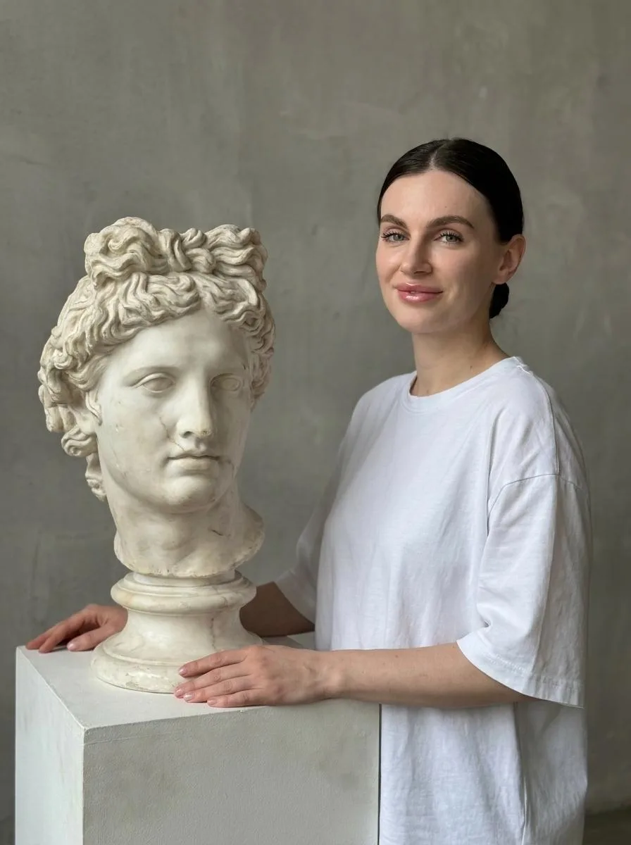 🖼 Woman stands facing a classical bust of apollo