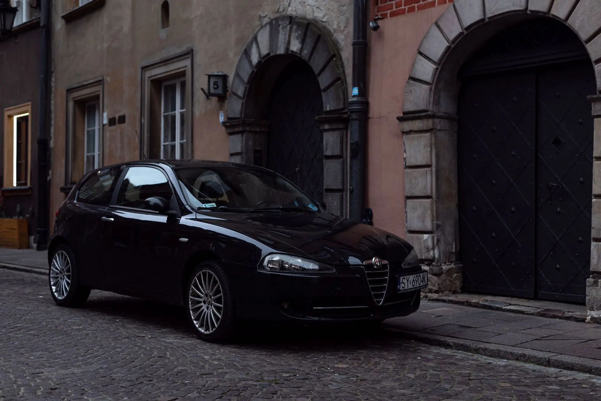 Alfa Romeo 147 в чёрном. Брусчатка, узкие улицы Варшавы и тёмные исторические фасады ос...