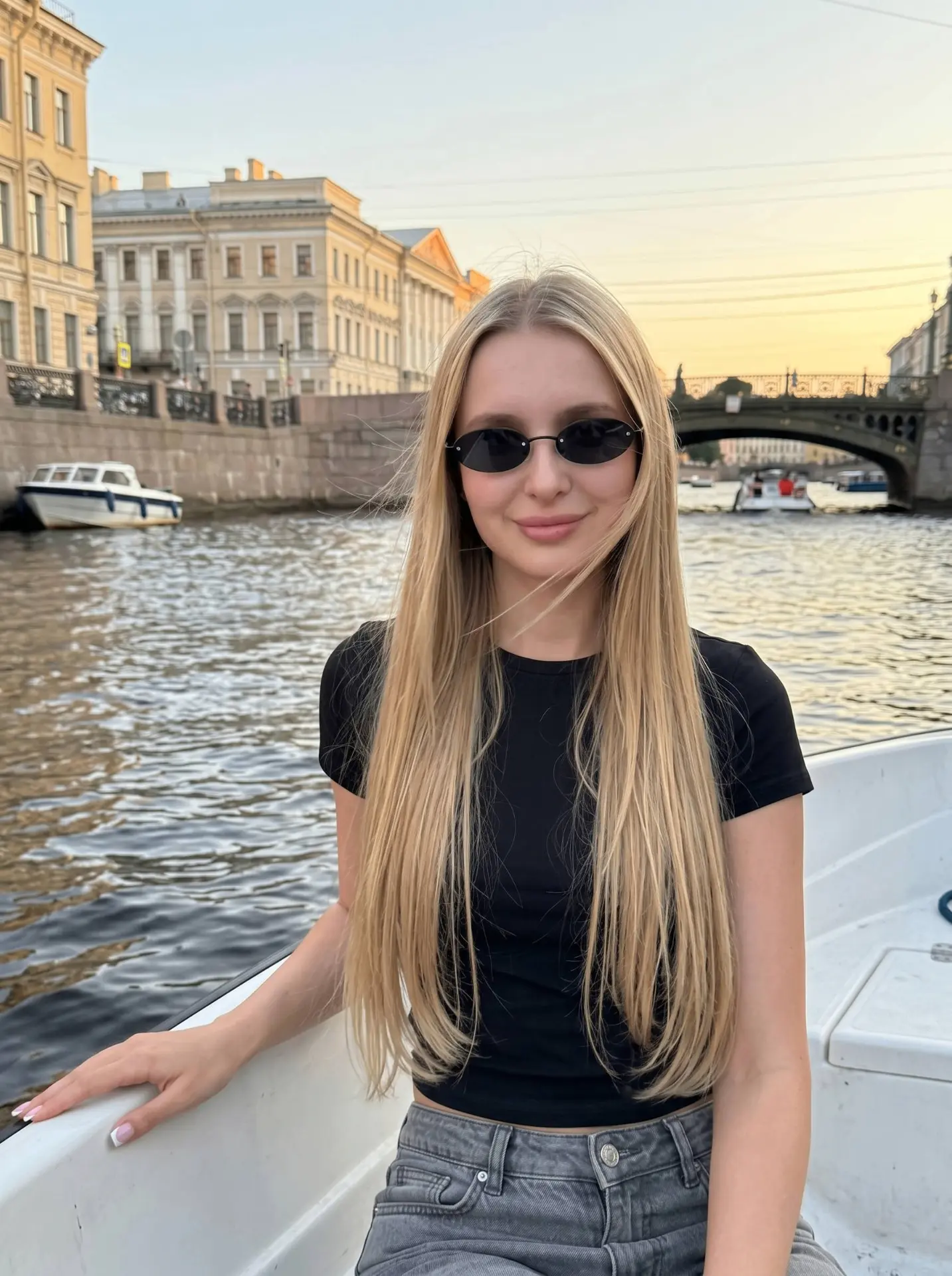 Девушка сидит в небольшой белой лодке на воде в Санкт-Петербурге, облокотившись рукой на борт и смот