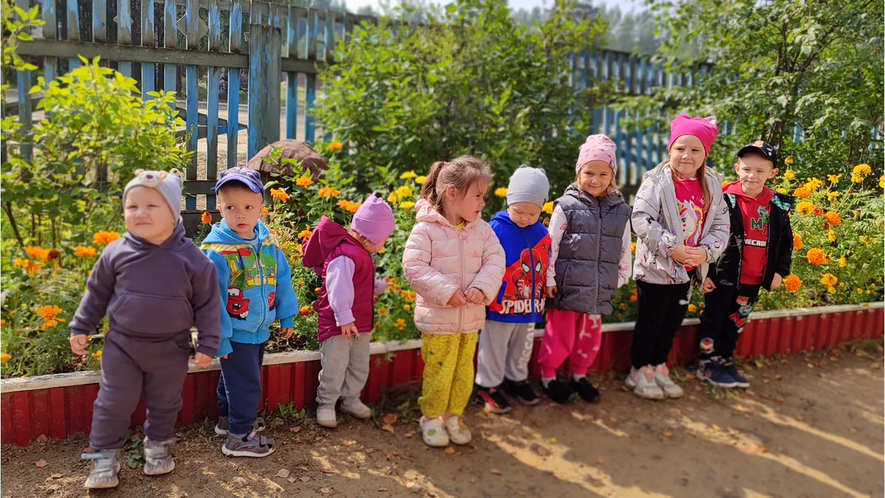 На прогулке дети дежурной группы наблюдали за цветами. на клумбах детского сада. Дети в...