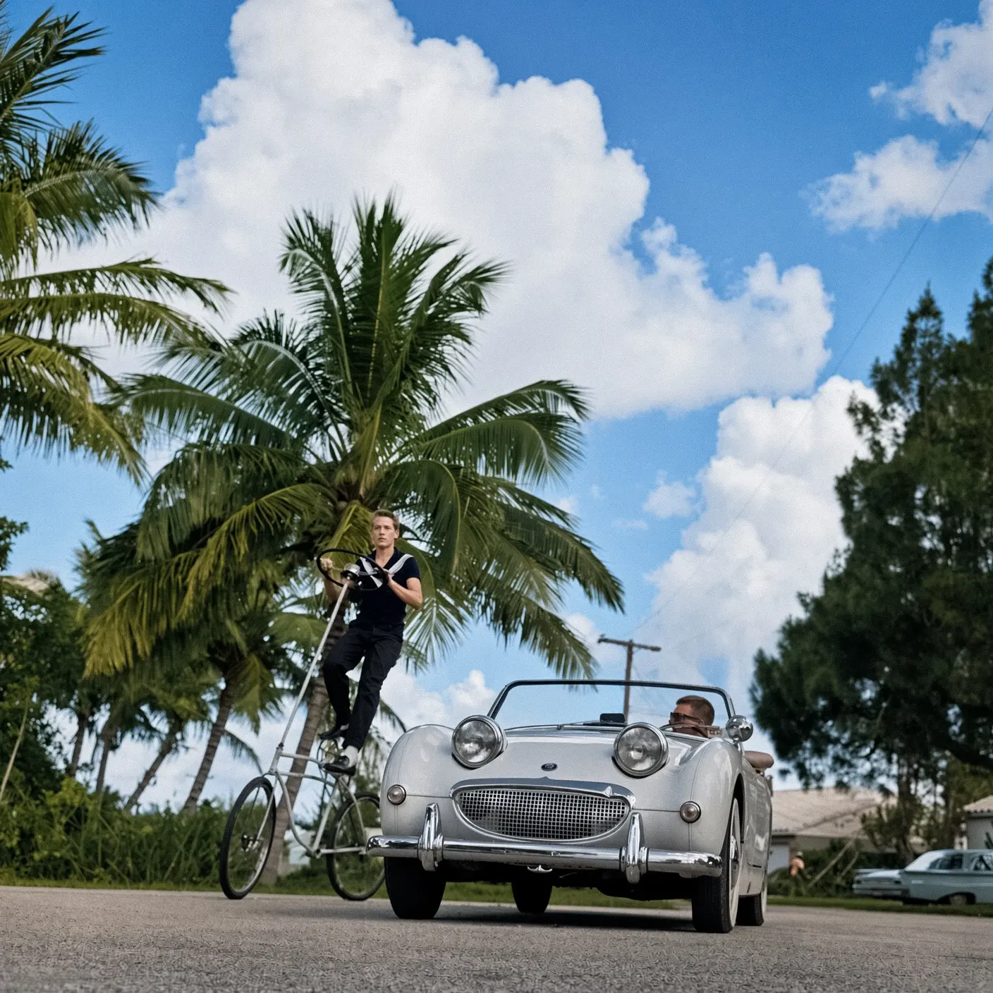 Велосипедист едет рядом с автомобилем Austin Healey Frogeye Sprite, США, около 1960 года.